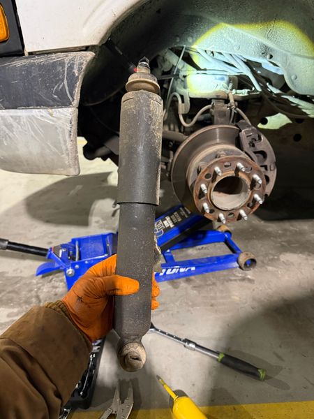 Technician holding a worn shock absorber in front of a truck wheel hub